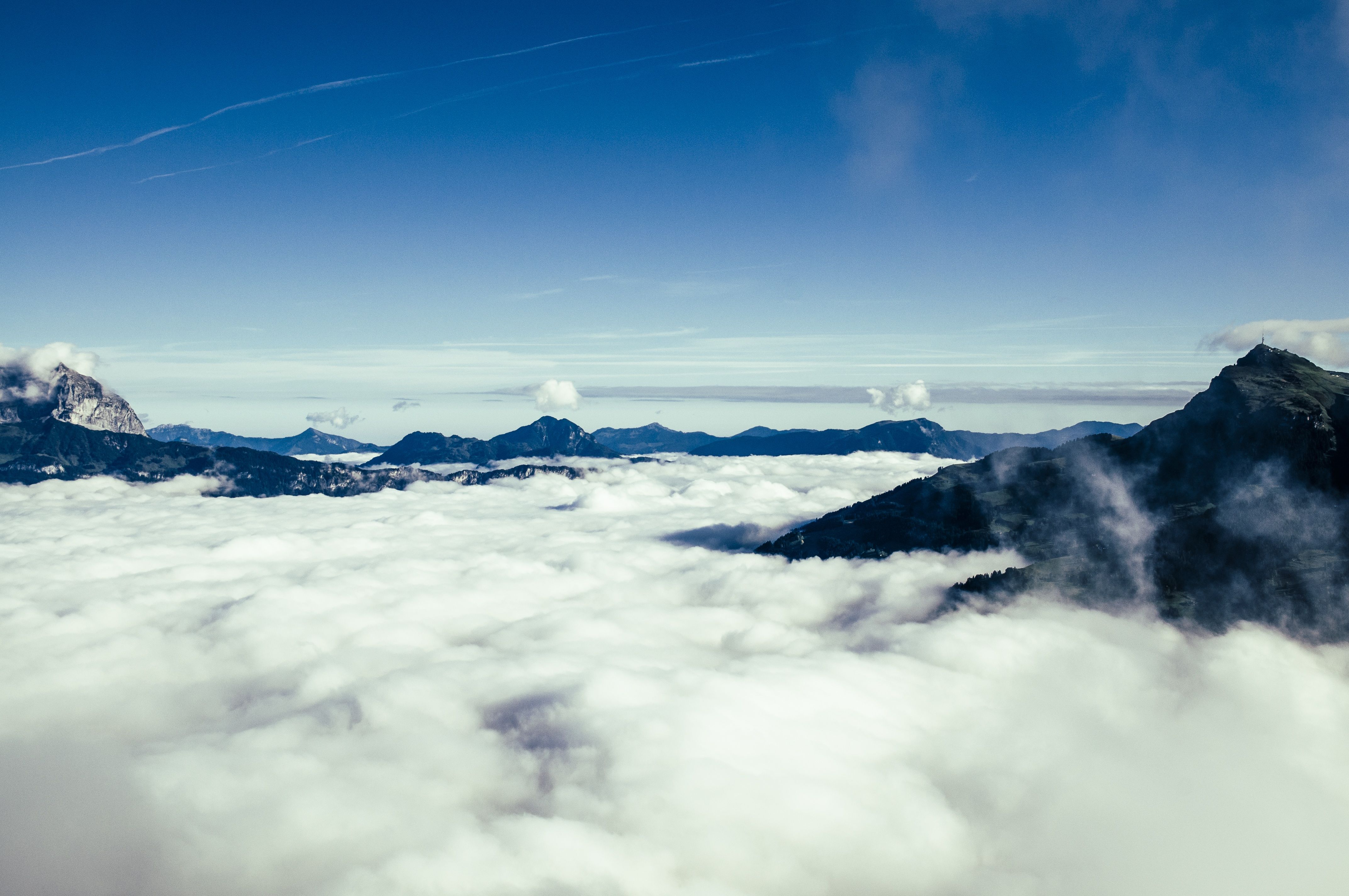 Dark mountain peaks rising above a dense white sea of clouds under a clear deep blue sky